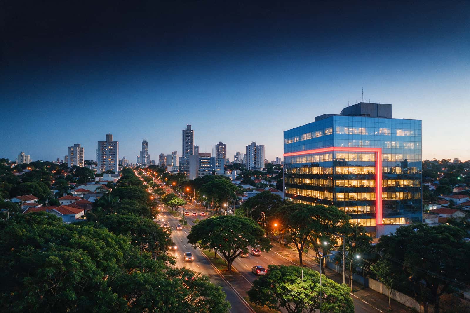 Vista elevada de uma cidade de porte médio ao anoitecer, com prédios comerciais e avenida arborizada